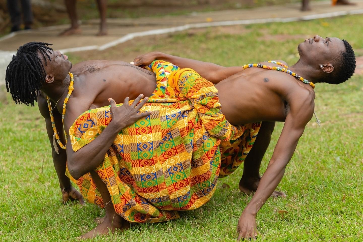 Two performers in Kente cloth dancing on grass